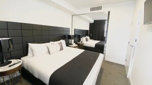 A modern hotel room with a large bed, a bedside table with a lamp, and a mirror on the wall.