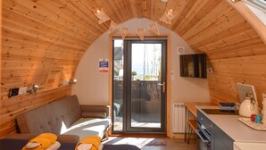 A cozy room with a wooden ceiling, a sofa, a table with a kettle, and a sliding glass door leading to an outdoor area. - Luxury Glamping Escape - Hot tub - West Coast Scotland (Innellan)