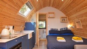 A compact, wooden interior with a kitchenette, a bed with blue bedding, and a small seating area. - Luxury Glamping Escape - Hot tub - West Coast Scotland (Innellan)