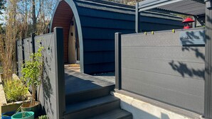 A modern outdoor structure with a wooden door and a blue roof, adjacent to a grey wall with a 'GANTOCKS' sign.