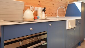 A kitchen with wooden paneling, a white kettle, a coffee maker, and a sink.