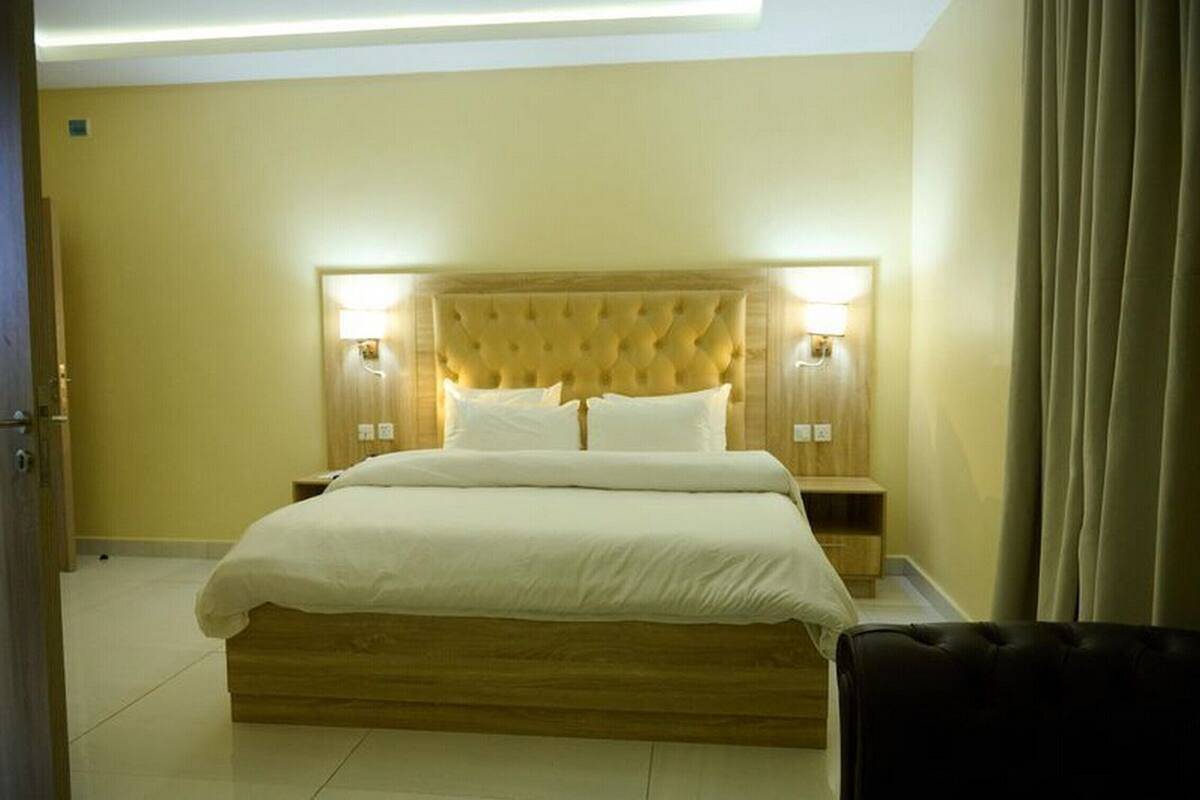 A neatly arranged bedroom with a large bed, wooden headboard, two bedside lamps, and a black leather chair.