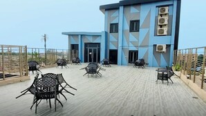 A building with a geometric facade, multiple air conditioning units, and outdoor seating with metal chairs and tables. - OTI Hotel Benin  (Benin City)
