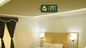 A hotel room with a large bed, a headboard with a tufted design, a bedside table with a lamp, and a chair. - OTI Hotel Benin  (Benin City)