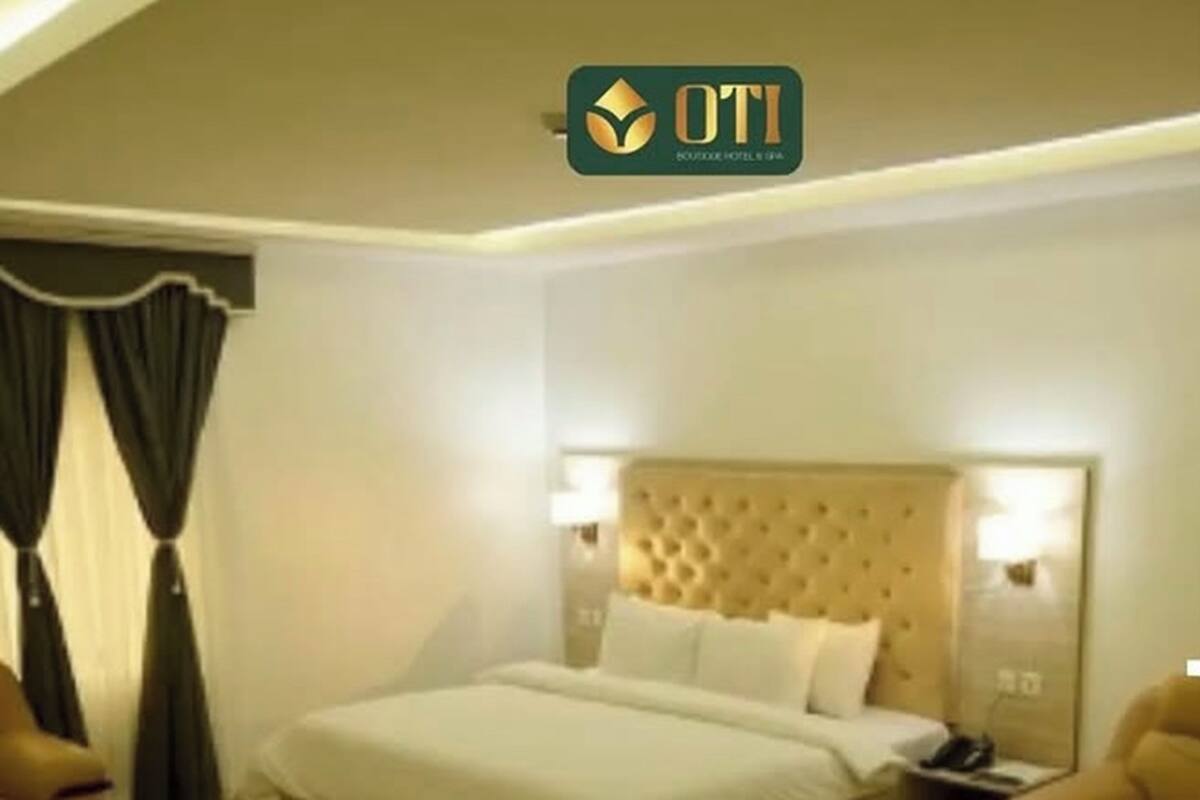 A hotel room with a large bed, a headboard with a tufted design, a bedside table with a lamp, and a chair.