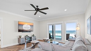 A modern living room with a large sofa, a ceiling fan, a flat-screen TV, and a view of the ocean through large sliding doors. - Bird of Paradise: Beachfront Views, Multiple Living Areas, Pet-Friendly (Mexico Beach)