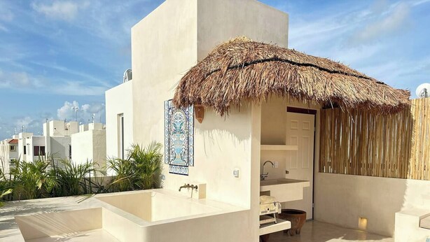 A modern outdoor bathroom with a thatched roof, a sink, and a small seating area.