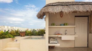 A modern outdoor kitchen with a thatched roof, a built-in sink, and a small seating area with a table and chairs.