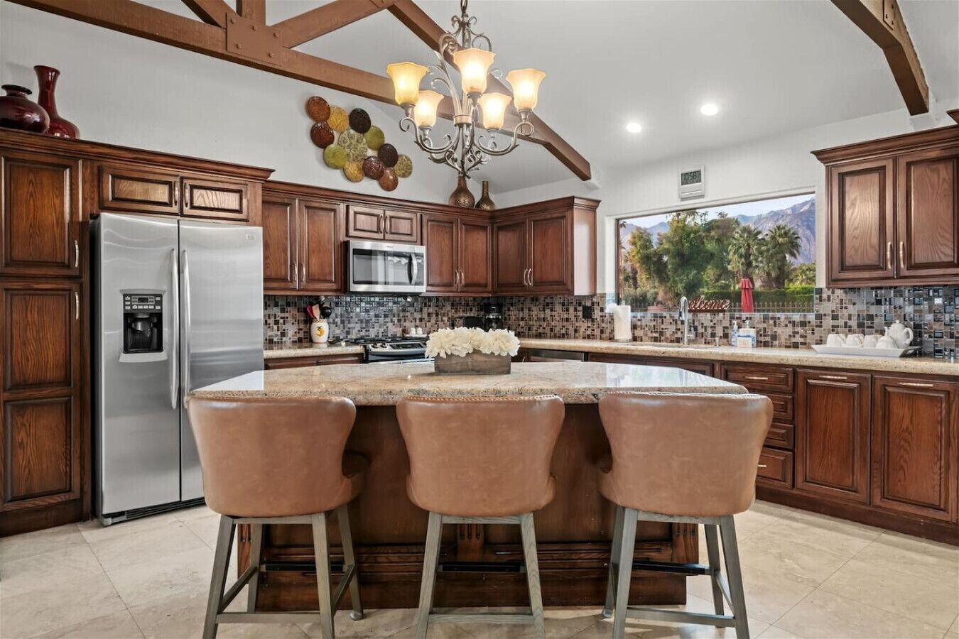 A kitchen with a central island, wooden cabinets, stainless steel appliances, and a chandelier.
