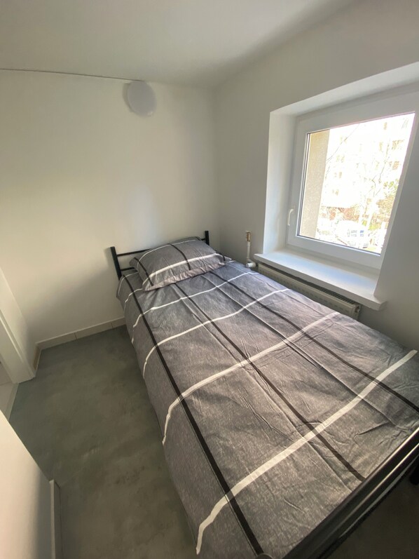 A single bed in a room with a window, white walls, and a radiator. - Hostel Harmonia (Warsaw)
