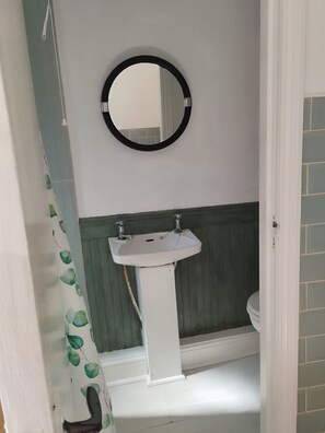 Un baño con un lavamanos blanco de pedestal, un espejo redondo y una pared verde.