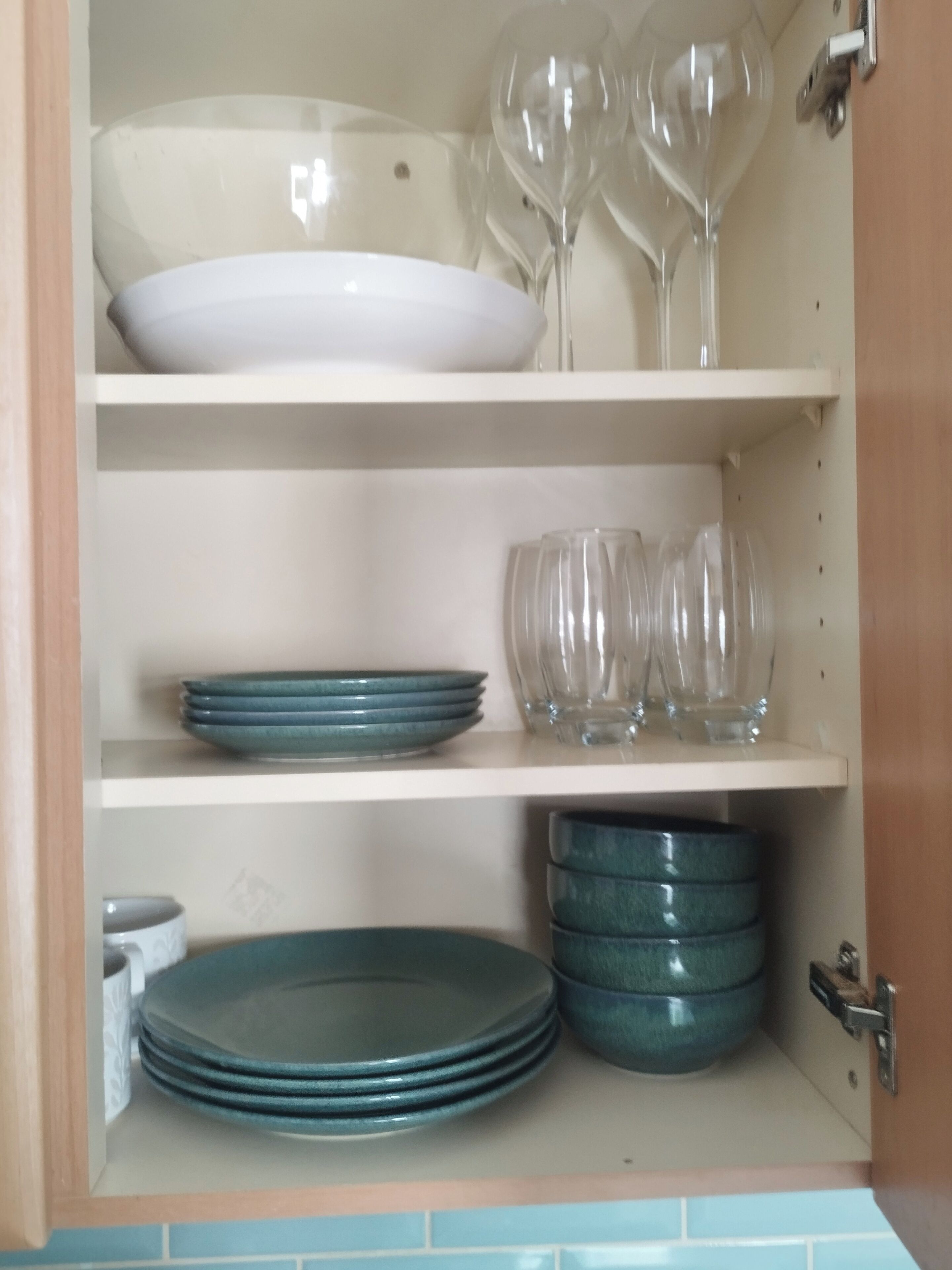 A kitchen cabinet with shelves holding plates, bowls, and wine glasses.