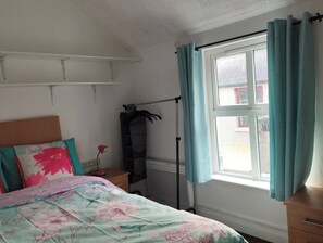 Un dormitorio con cama, radiador, ventana con cortinas, estante y armario.