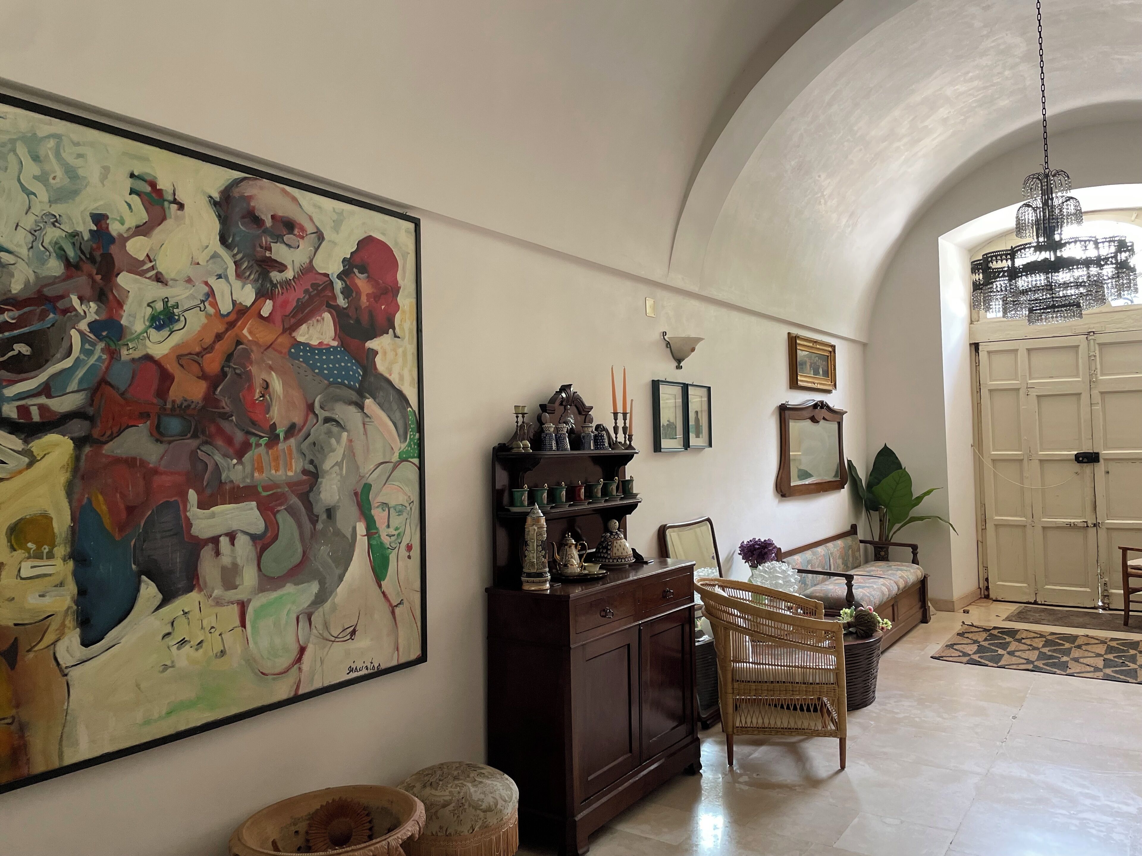 Un ampio corridoio con un grande quadro astratto, un mobile in legno scuro, mobili in vimini e un lampadario.