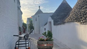 Una calle estrecha con edificios blancos, una moto estacionada al lado y una maceta con flores.