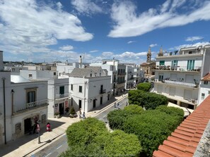 Vista de una calle en un pueblo con edificios blancos, una iglesia con campanario y un cielo azul despejado.
