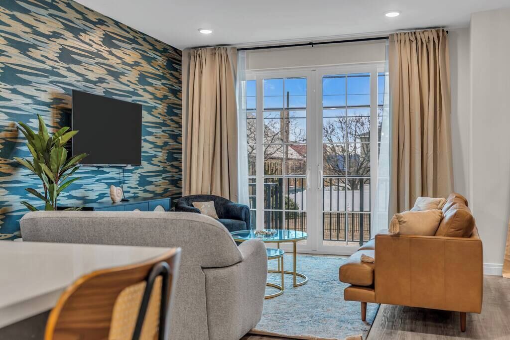 A modern living room with a sofa, armchair, and a dining area with a table and chairs.