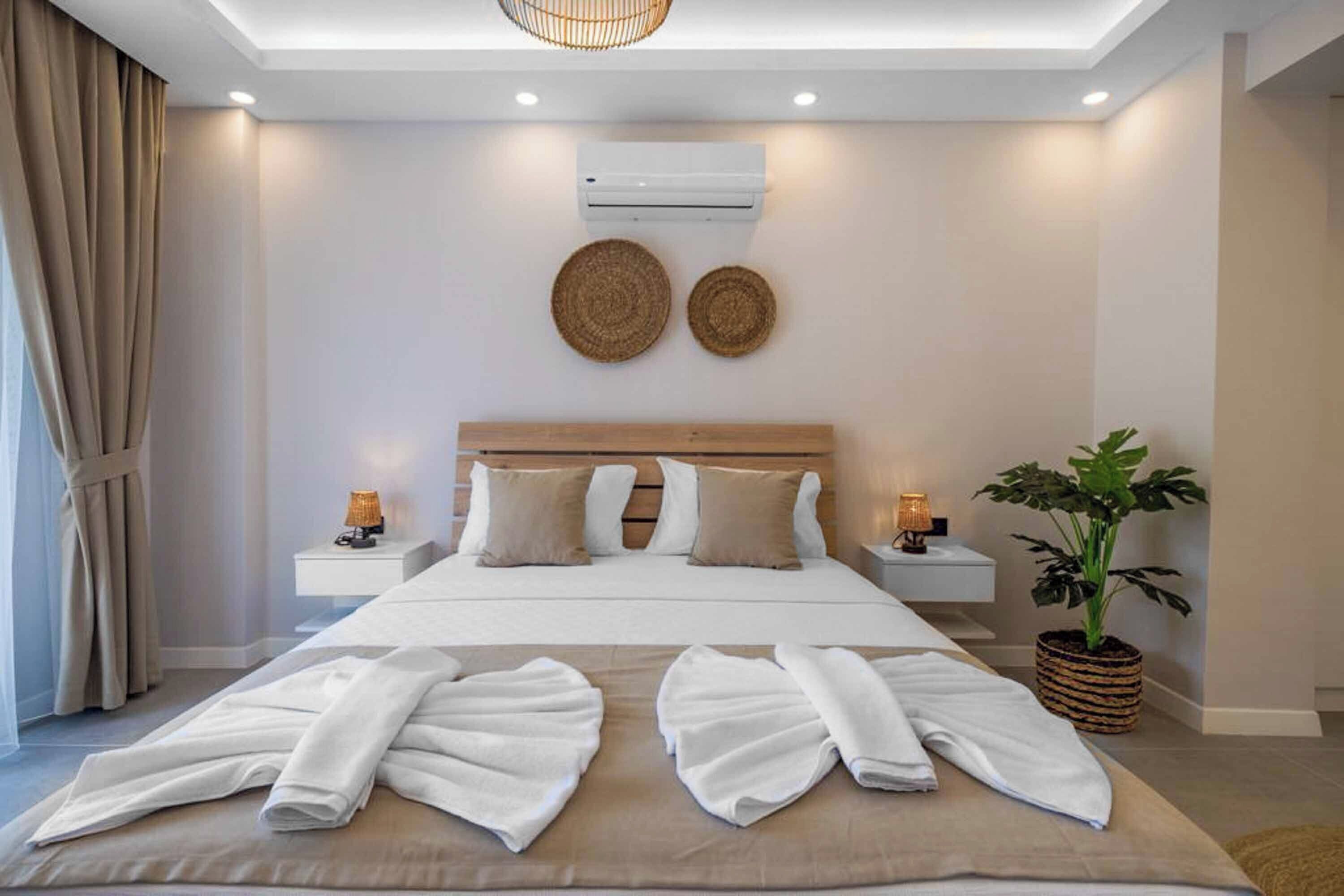A modern hotel room with a large bed, bedside tables with lamps, a potted plant, and a ceiling light fixture.