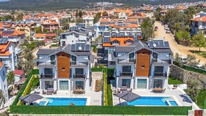 Uma área residencial moderna com várias casas de dois andares, uma piscina e montanhas ao fundo.