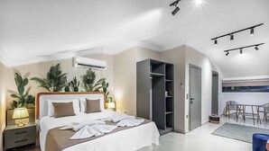 Una habitación de hotel moderna con una cama bien hecha, un armario, un escritorio con silla y un pequeño rincón de descanso.