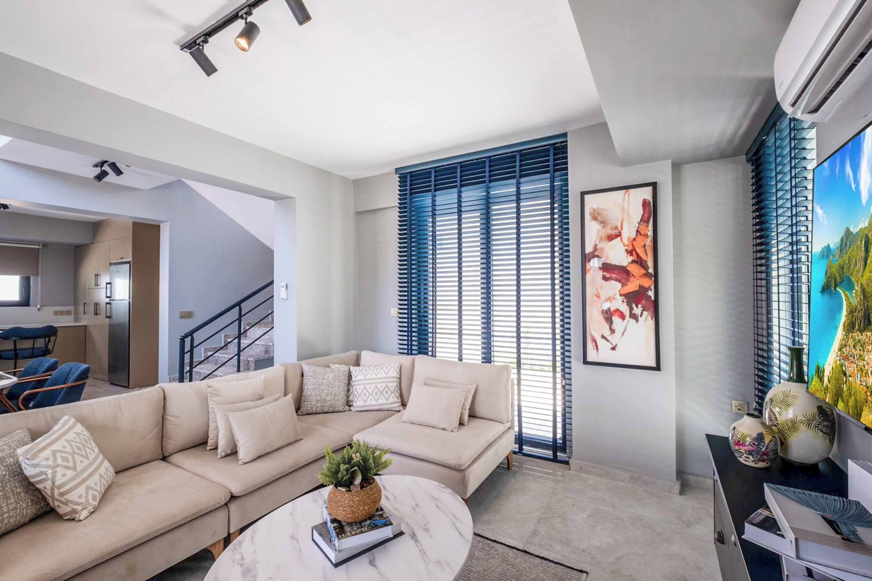 A modern living room with a beige sectional sofa, a marble coffee table, and a large flat-screen TV.