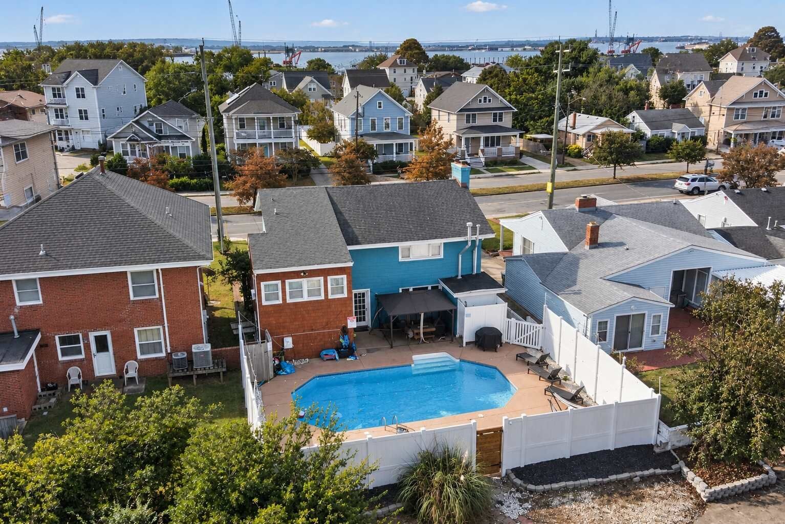Zona residencial con piscina rodeada de casas, vista despejada del agua y un puente distante.
