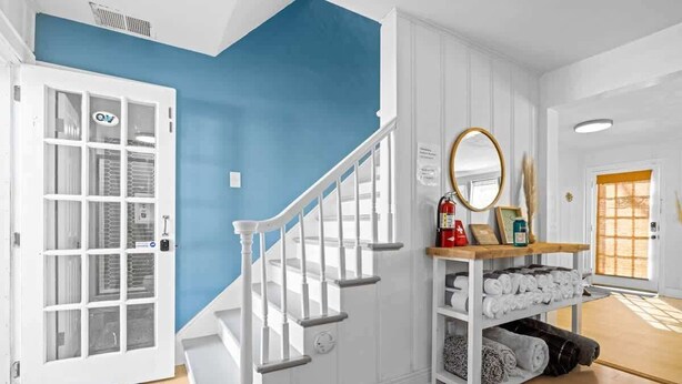 A staircase with white railings and a blue wall. There is a white door with glass panels and a fire extinguisher on a shelf. - Coastal home w/ pool, hot tub & fire pit (Norfolk)