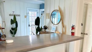 A kitchen with a bar area, two black bar stools, a hanging light fixture, a globe, and a fire extinguisher. - Coastal home w/ pool, hot tub & fire pit (Norfolk)