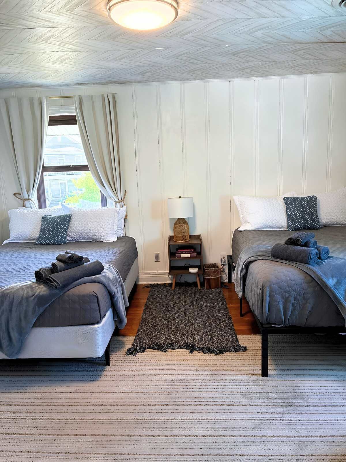 Une chambre avec deux lits, une table de chevet avec une lampe et une fenêtre avec des rideaux.