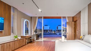 Ein modernes Hotelzimmer mit einem großen Bett, einem Schreibtisch mit Stuhl, einem Fernseher und Blick auf die Stadt im Abendrot.