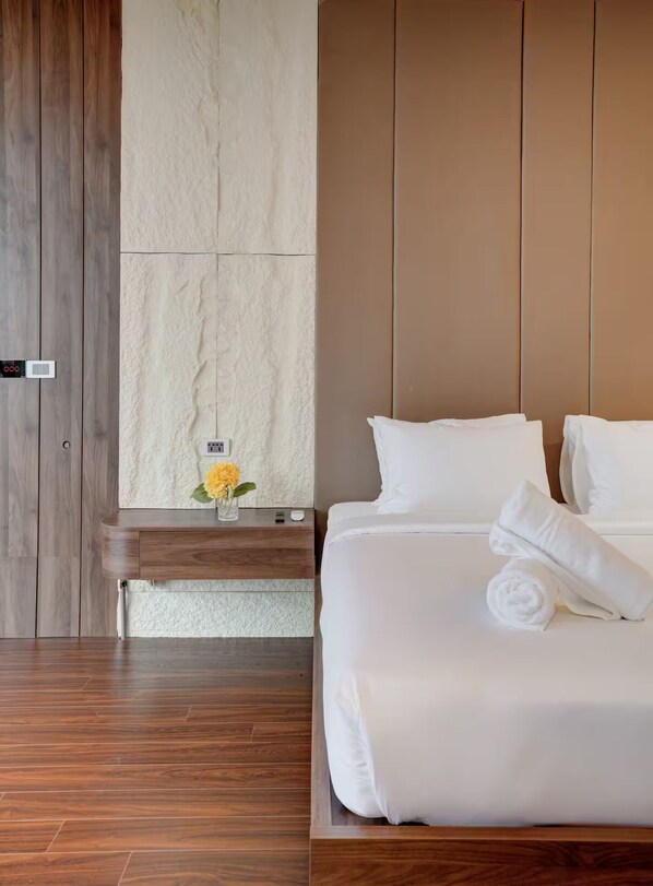 A hotel room with a wooden floor, a bed with white linens, a nightstand with a vase of flowers, and a textured wall.