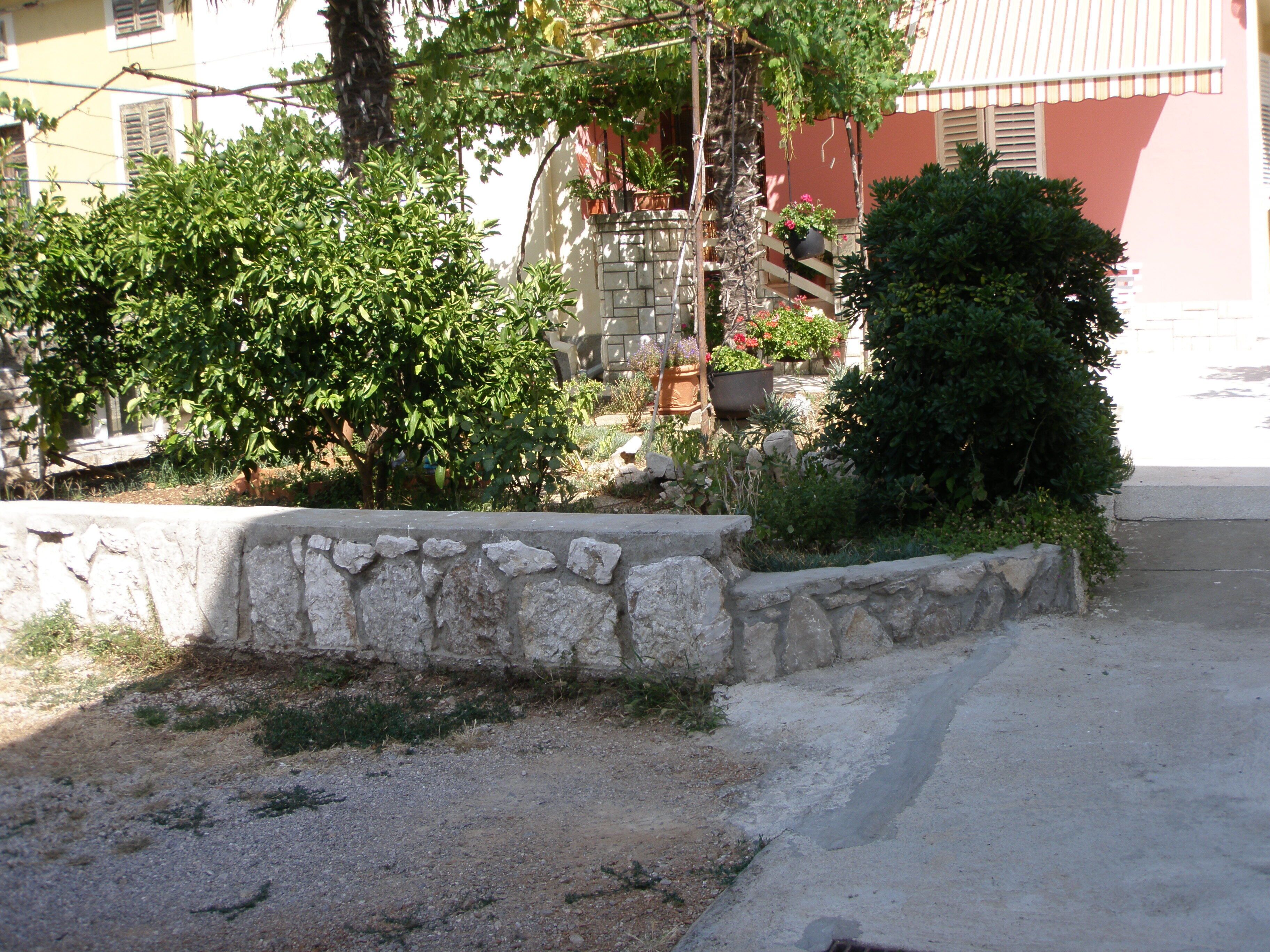 A stone retaining wall with greenery and a building in the background.