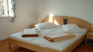 A neatly made bed with folded towels, a bedside lamp, and a wooden headboard in a room with wooden flooring. - Apartman Žardin with AC and balcony (Punat)