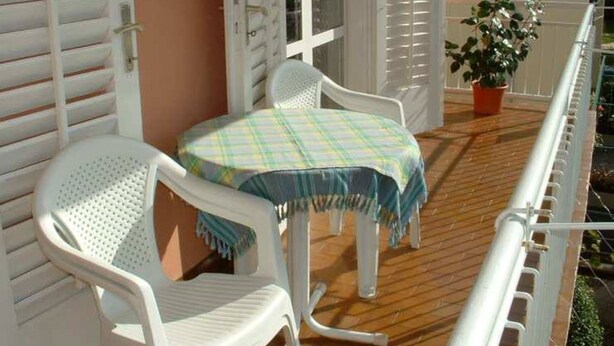 A balcony with a white chair, a small table with a checkered tablecloth, and a potted plant with red flowers. - Apartman Žardin with AC and balcony (Punat)
