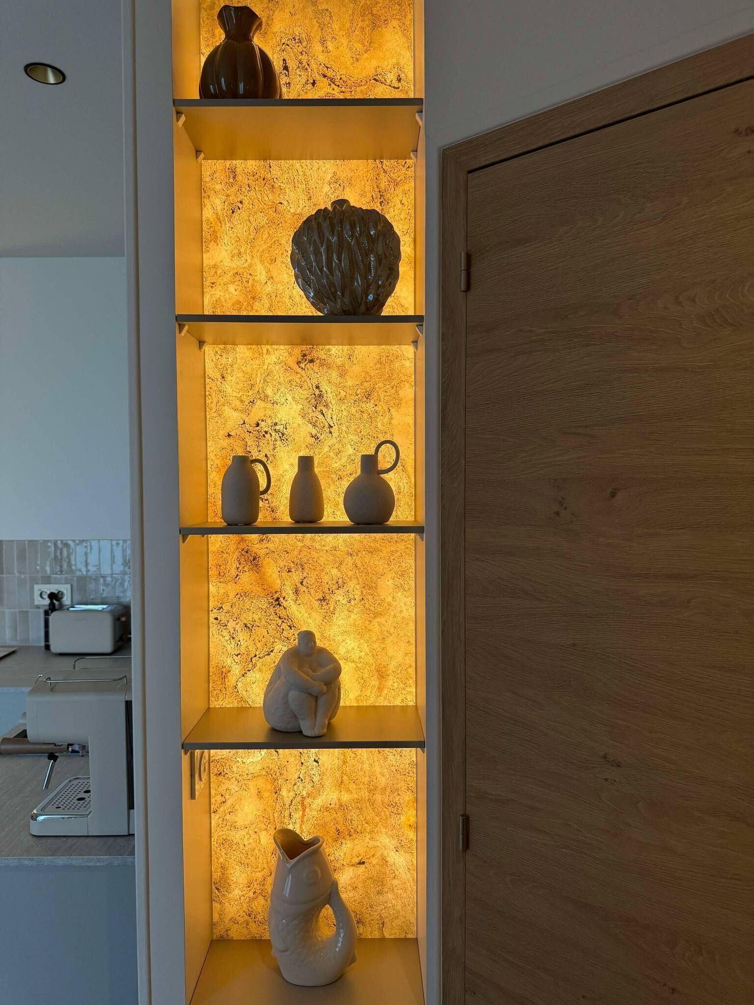 A kitchen with a built-in shelf unit displaying various ceramic vases and a sculpture.