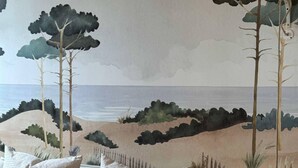 A bedroom with a beach mural, a bed with white bedding, and a bedside lamp.