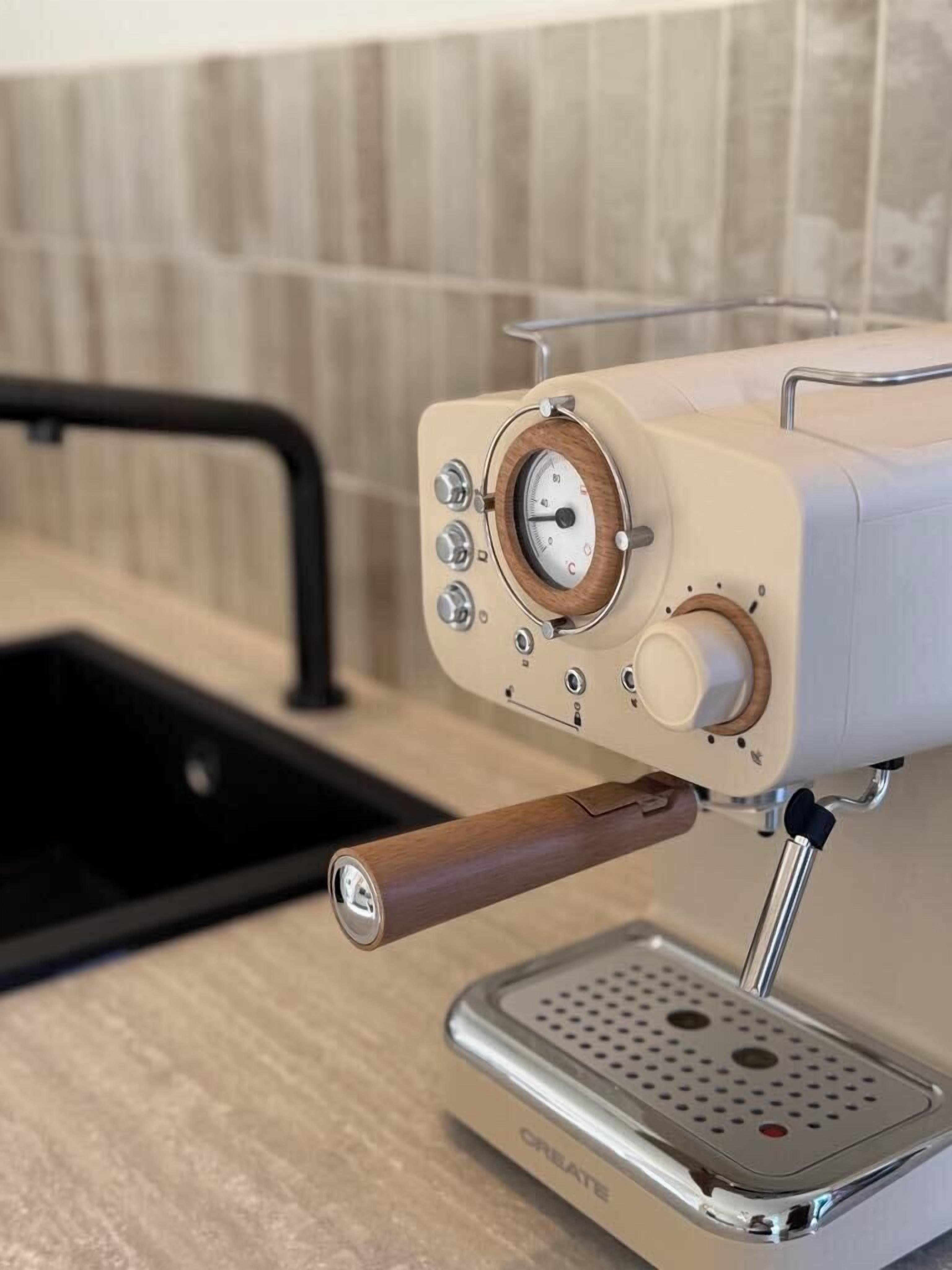 Et køkken med kaffemaskine, vask og flisebeklædt væg.