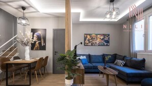 A modern living room with a dining area, a blue sofa, and a staircase.