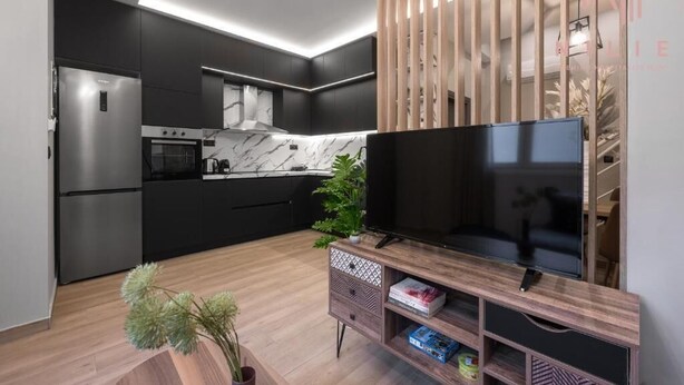 A modern kitchen with a built-in oven, microwave, and a large flat-screen TV on a wooden stand.
