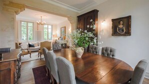 Ein Esszimmer mit einem großen Holztisch, gepolsterten Stühlen und einer Vase mit Blumen.