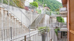 A multi-level outdoor staircase with metal railings, surrounded by greenery and leading to a building with a stone facade.