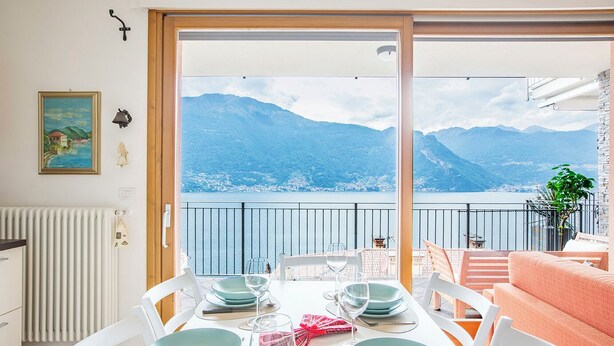 A dining area with a table set for four, overlooking a lake with mountains in the background.