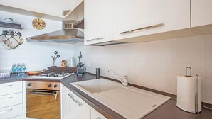 A modern kitchen with white cabinets, a gas stove, a sink, and a coffee machine.