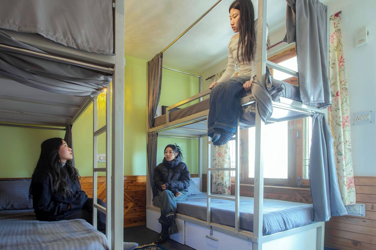 A dormitory room with bunk beds, a window with curtains, and a wooden floor.