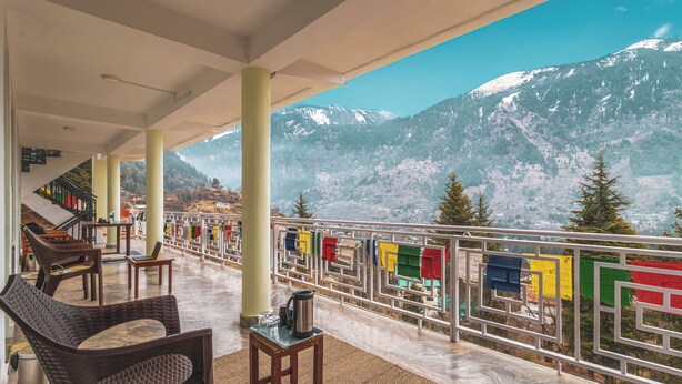 Een balkon met zitplaatsen, een uitzicht op besneeuwde bergen en gebedsvlaggen.
