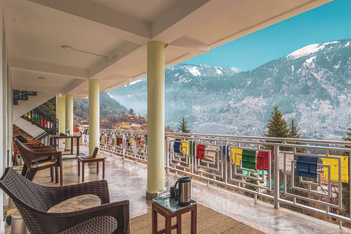A balcony with seating, a view of snow-capped mountains, and prayer flags.