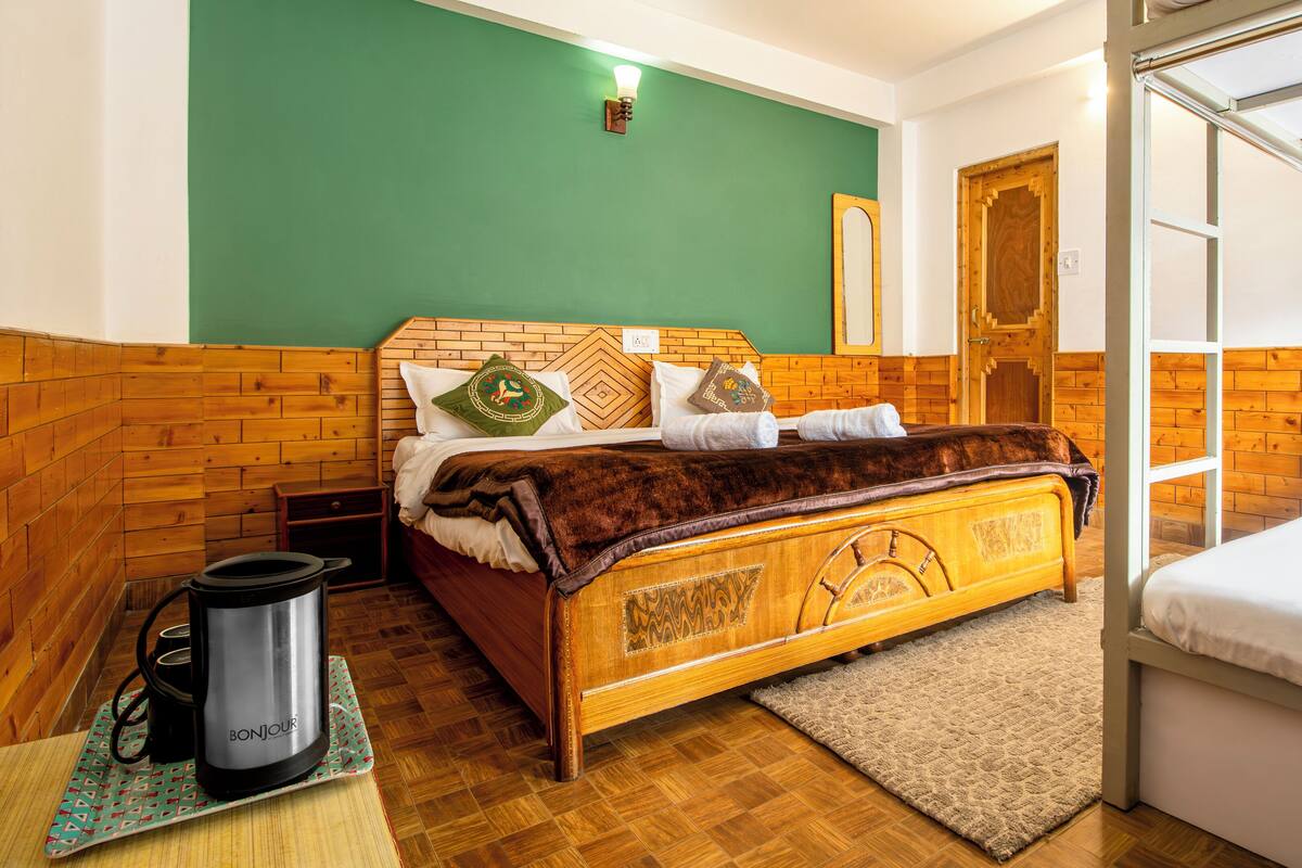 A hotel room with a wooden headboard, a bed with white linens, a small table with a kettle, and a green wall.