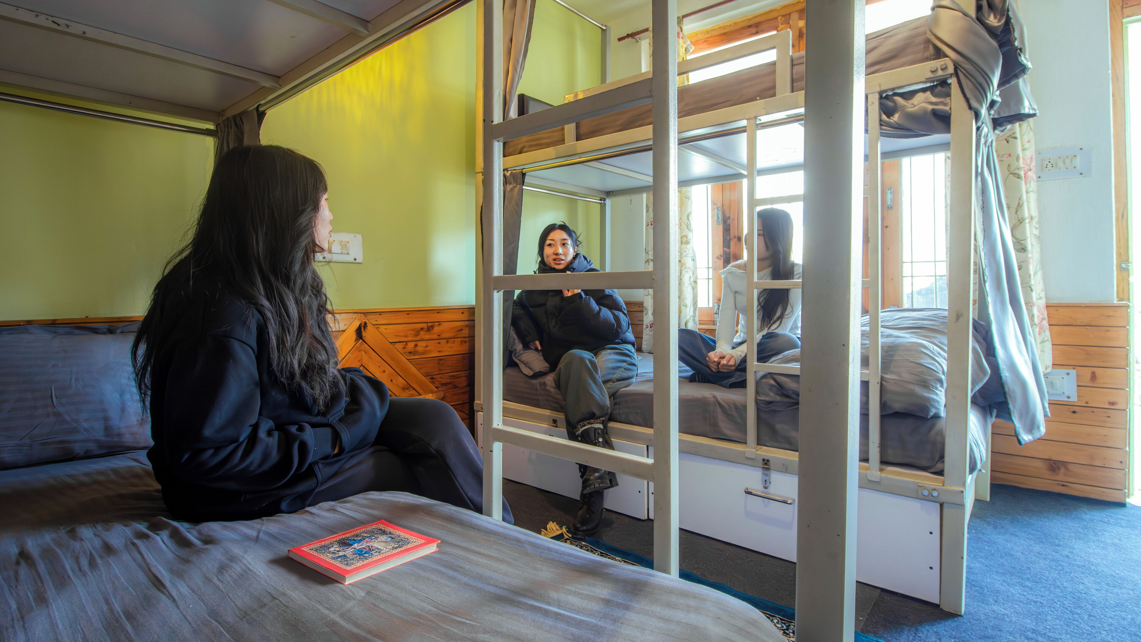 Une chambre avec un lit superposé, une personne assise sur le lit du bas et une autre sur le lit du haut.