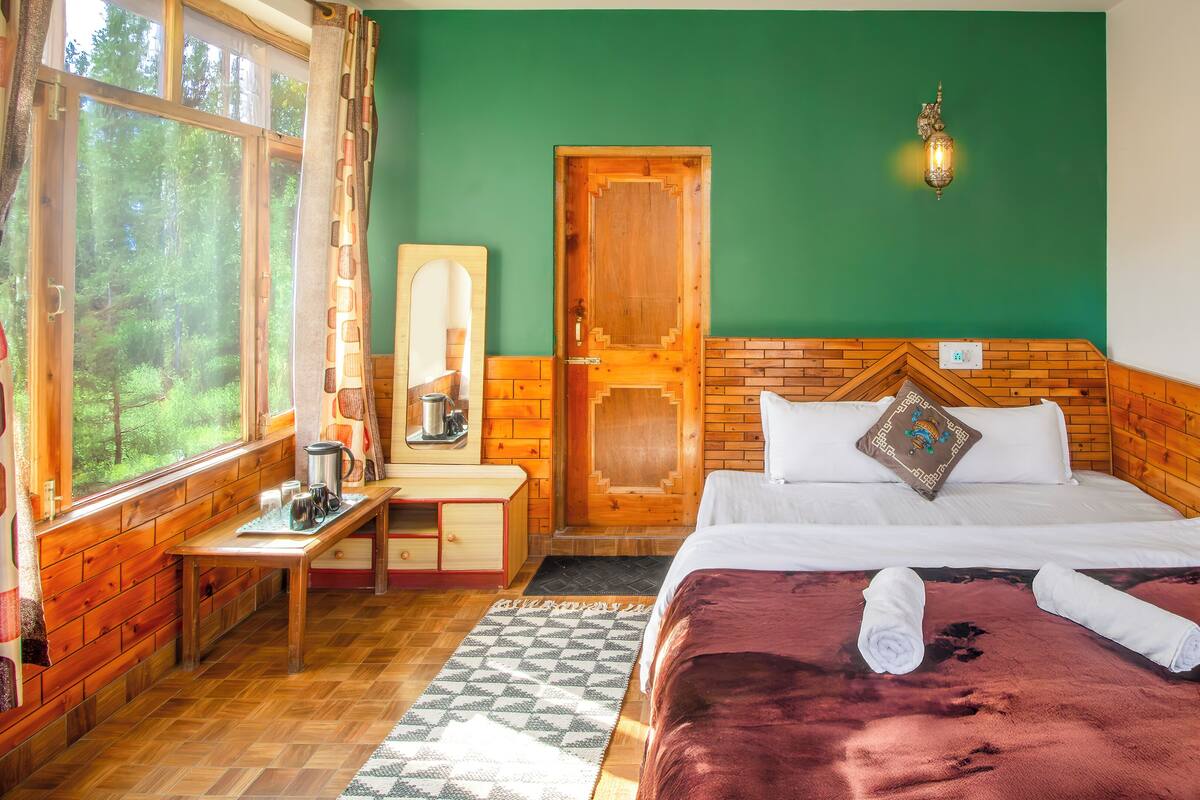 A room with a bed, a wooden desk, a mirror, and a window with curtains.