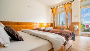 Een hotelkamer met een houten hoofdbord, een groot bed met wit en bruin beddengoed, een raam met gordijnen en uitzicht op bergen.